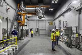 Vista interior de la celda de prueba del grupo electrógeno que incluye un patín de combustible diésel, paneles de control localizados y un brazo de escape del motor ajustable.